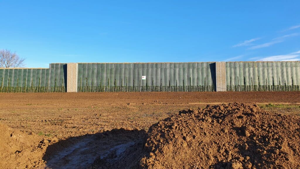 Laermschutzwand-mit-gruener-Bepflanzung-davor-eine-Baustelle-mit-Erdarbeiten
