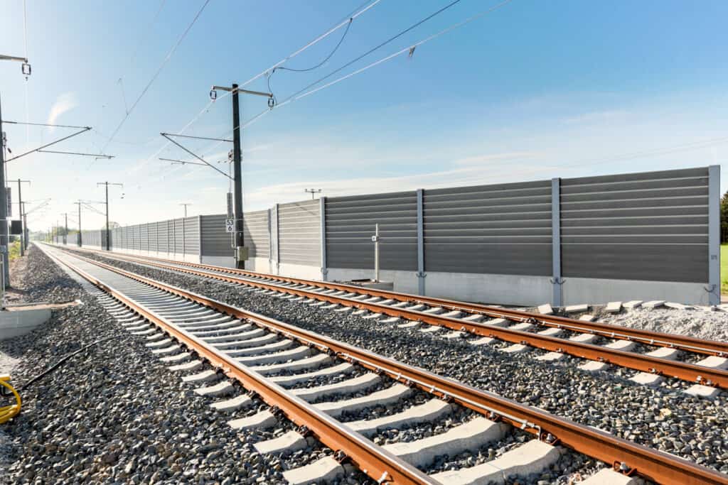 Bahngleise-mit-Oberleitungen-verlaufen-entlang-einer-hohen-Schallschutzwand