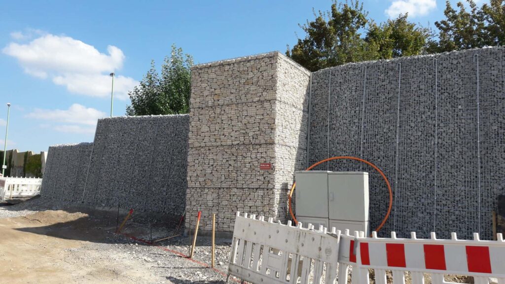 rau-klimawand-alpin-Baustelle-mit-hoher-Laermschutzwand-aus-Steinkoerben
